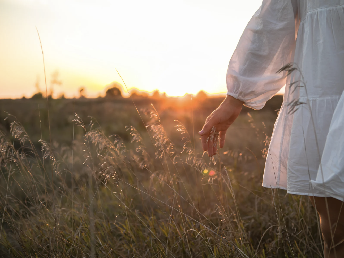 Woman walking trough tall grass with arm outstretched